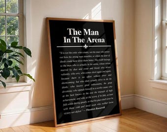 May include: A rectangular wall art print in a thin gold frame featuring a black background with white text. The title reads The Man In The Arena, followed by the full Theodore Roosevelt quote and a small fleur-de-lis symbol centered below the title.