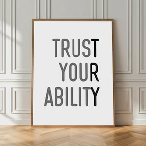 May include: A framed print with the words "TRUST YOUR ABILITY" in a bold, sans-serif font. The text is arranged in three lines, with the word "TRUST" in black, "YOUR" in gray, and "ABILITY" in black. The print is displayed against a white wall.