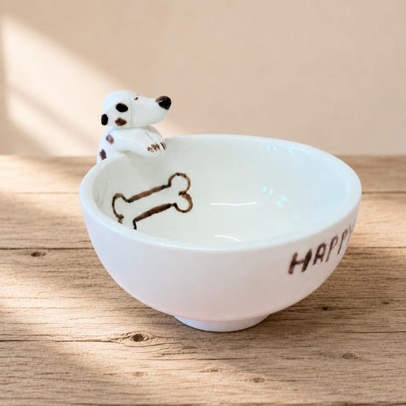 A hand-sculpted ceramic bowl shaped like a cheerful spotted pup — functional ring dish that doubles as a tiny piece of character art on your nightstand.