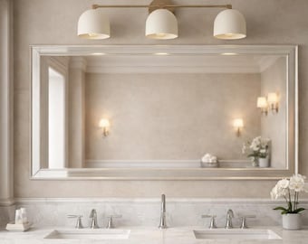 May include: A bathroom vanity with a large rectangular mirror and a three-light fixture. The light fixture has a gold finish and white dome-shaped shades. The vanity has a marble countertop, two sinks, and gray cabinets.