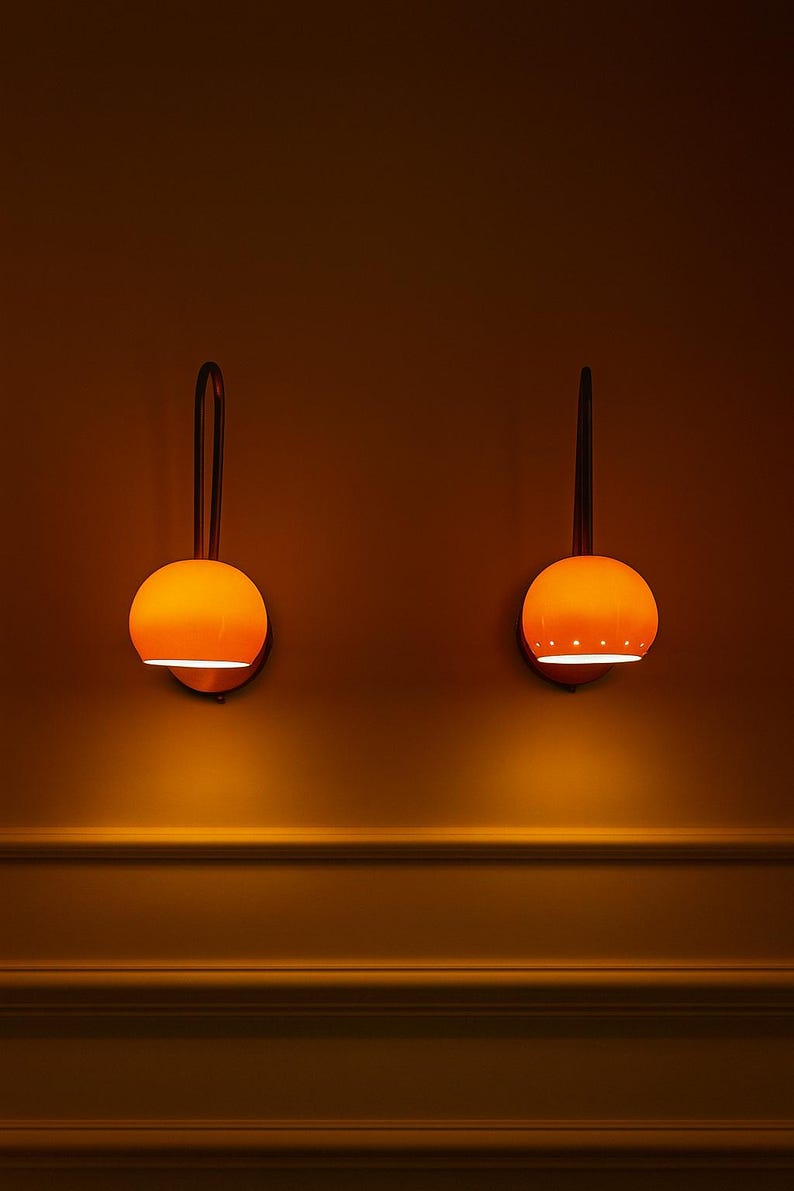 May include: Two orange globe-shaped wall sconces with a dark brown curved arm and a circular base. The sconces are mounted on a warm-toned wall. The sconces emit a warm glow, creating a cozy ambiance.