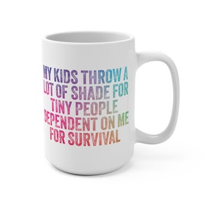 May include: White ceramic mug with a large handle. The mug features the text "MY KIDS THROW A LOT OF SHADE FOR TINY PEOPLE DEPENDENT ON ME FOR SURVIVAL" in a rainbow gradient.