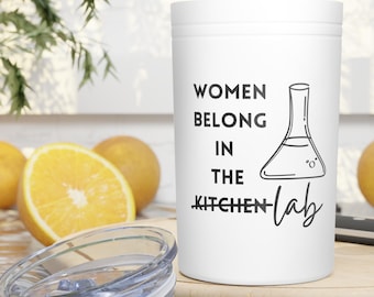 May include: White tumbler with a black graphic that says "Women belong in the kitchen lab" with a drawing of a beaker.
