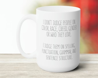 Könnte beinhalten: Eine weiße Keramik-Kaffeetasse mit einer schwarzen Textnachricht, die lautet: "Ich beurteile Menschen nicht nach ihrer Hautfarbe, Rasse, ihrem Glauben, ihrem Geschlecht oder wem sie lieben. Ich beurteile sie nach ihrer Rechtschreibung, Zeichensetzung, Grammatik und Satzstruktur."