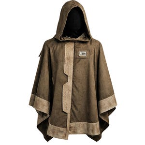 Peut inclure: Un poncho à capuche marron avec un aspect texturé. Le poncho présente une bordure contrastante marron clair sur les bords et sur le devant. Un petit patch carré avec du texte est visible sur la poitrine. La capuche est doublée de tissu noir.
