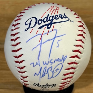 Può includere: Una palla da baseball bianca Rawlings con cuciture rosse, il logo blu dei Dodgers e un autografo a inchiostro blu. La palla presenta la scritta a mano 77, 24 WS MVP e la firma di Mookie Betts sotto il logo della squadra e sopra il marchio Rawlings.