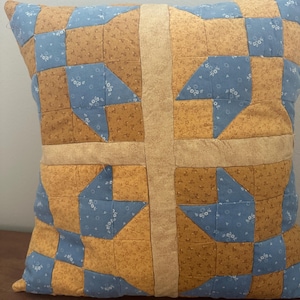 Può includere: Un cuscino quadrato con un design patchwork nei toni del giallo senape e del blu polvere. Il tessuto presenta una piccola stampa floreale su tutta la superficie, con una fascia solida color marrone chiaro verticale e orizzontale al centro.
