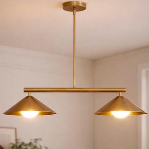 Puede incluir: Una lámpara colgante de dos luces de color latón. La lámpara tiene una varilla central fijada al techo, con una barra horizontal que sostiene dos pantallas cónicas. Cada pantalla tiene una bombilla brillante.