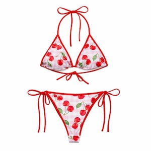 May include: A two-piece bikini set with a red and white gingham pattern and a cherry print. The halter-neck top and classic-cut bottoms are trimmed and tied with red. A summery swimwear item.