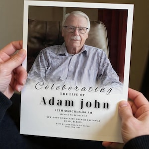 May include: A memorial card held in hands, with a portrait of a man in glasses and a striped shirt. The card reads "Celebrating the Life of Adam John" with service details, including the date and time.