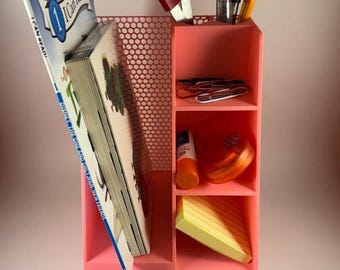 May include: A pink desk organizer with multiple compartments and a drawer. It holds a book, scissors, pens, paperclips, a glue stick, a round container, sticky notes, and colorful markers. The book reads "I Can Read!"