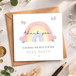 May include: A square greeting card featuring a watercolour rainbow design and the words "thank you" in script. The card also includes the text "FOR BEING THE BEST TEACHER" and "MISS SMITH". The card is on a brown envelope.