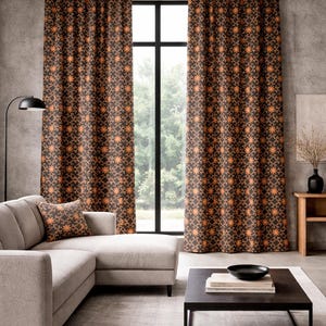 May include: Brown and orange patterned curtains hang in front of a window. A matching throw pillow rests on a light gray sectional sofa. The room has a modern, minimalist design with a dark coffee table and a black lamp.
