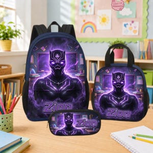 Może przedstawiać: Ciemnoniebieski zestaw składający się z plecaka, torby na lunch i piórnika z grafiką postaci Black Panther otoczonej fioletową energią. Każdy element zawiera napis Zion fioletowymi literami na tle przedstawiającym salę lekcyjną.