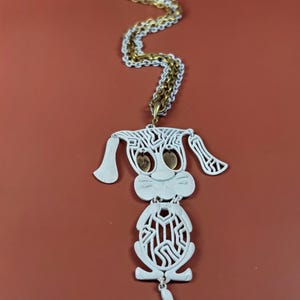 May include: A vintage necklace featuring a white dog pendant with a gold and white chain. The dog pendant has a cut-out design with gold-colored eyes. The chain is a mix of gold and white links.