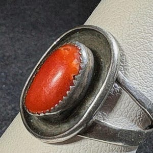 May include: A silver ring featuring an oval, vibrant orange gemstone. The gemstone is set within a detailed, textured bezel. The ring's band is a simple, polished silver design. This piece is a statement accessory.
