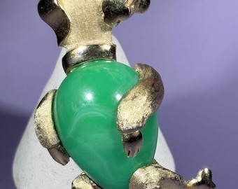 May include: A vintage poodle brooch. The gold-tone metal poodle has a green, marbled, oval-shaped centre. The poodle is upright, with textured gold detailing on its head and legs. A classic accessory.