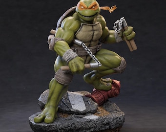 May include: A detailed statue of Michelangelo from the Teenage Mutant Ninja Turtles. The figure is green with an orange mask, holding nunchucks. The statue is posed on a rocky base with a red fire hydrant.