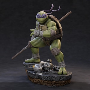 May include: A detailed figurine of Donatello from Teenage Mutant Ninja Turtles. The green turtle figure is posed with a bo staff, wearing a purple mask and brown armour. The figure stands on a rocky base with debris. The overall design is highly detailed.