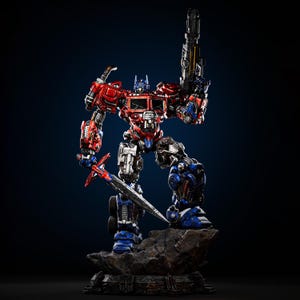 May include: A detailed action figure of Optimus Prime, a red, blue, and silver robot, holding a sword and a blaster. The figure stands on a rocky base against a dark blue background. The robot's design features intricate mechanical details.