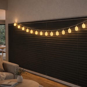 Könnte beinhalten: Eine Lichterkette mit warmweißen, laternenförmigen Lichtern hängt vor einer dunklen Wand. Die Lichter sind gleichmäßig verteilt und strahlen ein sanftes Leuchten aus, wodurch eine gemütliche Atmosphäre entsteht. Die Szene zeigt ein Wohnzimmer mit Sofa und Couchtisch.