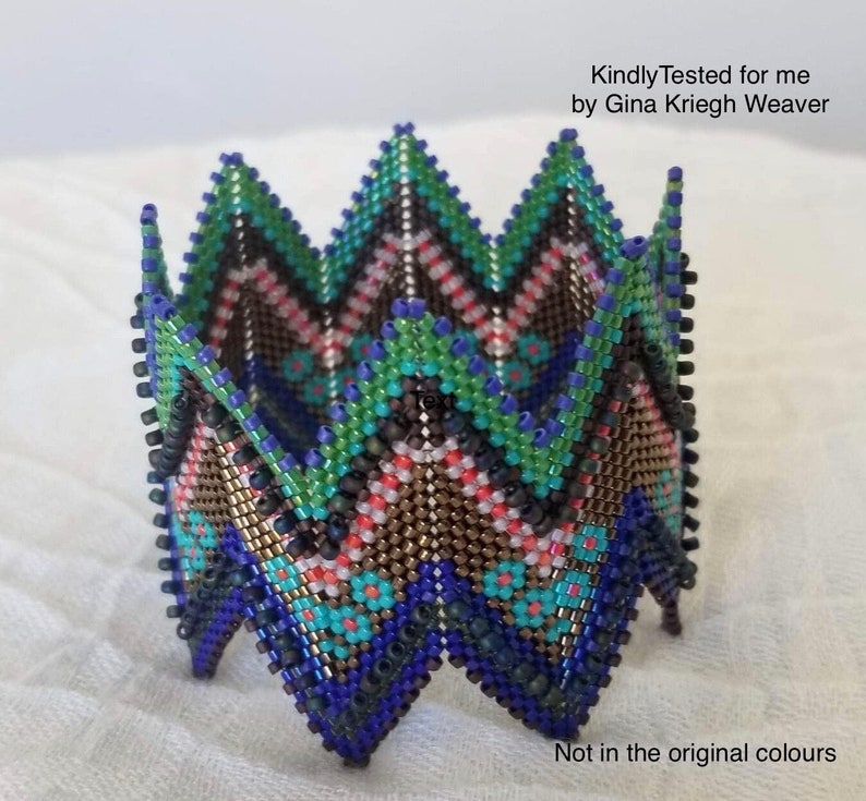 May include: A beaded, geometric, multi-coloured, folded, decorative piece. The piece is made of small, colourful beads in shades of blue, green, brown, pink, and orange. The piece is folded into a star shape. "Kindly Tested for me by Gina Krieg Weaver" and "Not in the original colours" are written in the image.