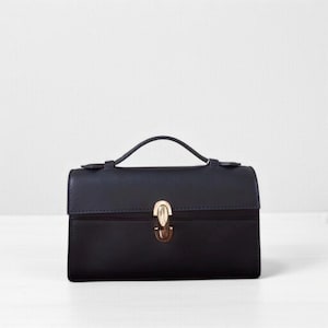 May include: A black handbag with a top handle and a gold-coloured clasp. The rectangular bag has a flap closure and a small handle for carrying. The bag is set against a white background.