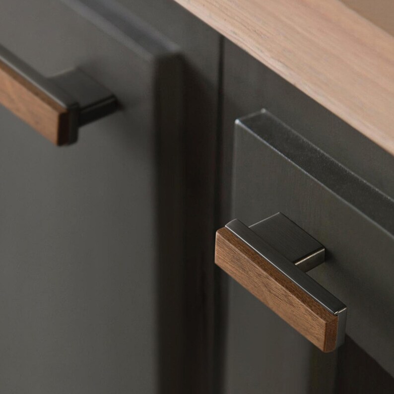 May include: Close-up of dark grey cabinet doors with rectangular, modern hardware. The hardware features a combination of dark metal and wood, with a light wood accent on the handle. A light wood countertop is visible.