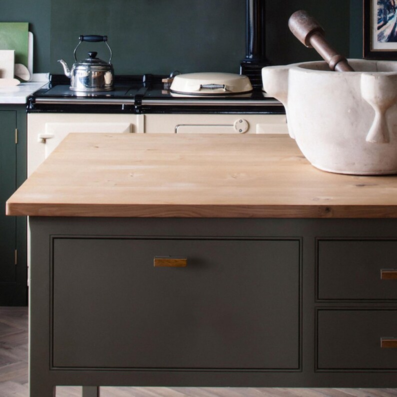 May include: A kitchen island with a light wood countertop and dark grey cabinets. A stainless steel kettle sits on a cream-coloured stove. A large white mortar and pestle are on the countertop, with a wooden pestle inside.
