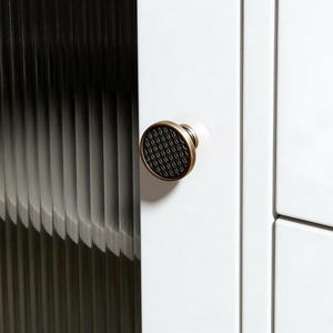 May include: A white ceramic mug with a black handle and the text "But First, Coffee" in a bold, black font. The mug is set against a blurred background, suggesting a cozy setting.