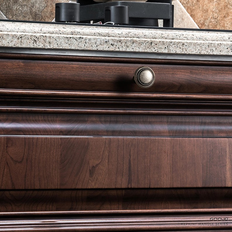 May include: Close-up of a dark brown wooden cabinet drawer with an antique-style knob. The drawer features a detailed wood grain and a curved design. The knob is a muted gold colour.