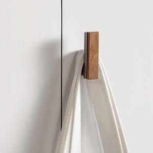 May include: A rectangular wooden hook with a dark brown finish is mounted on a white surface. A white towel hangs from the hook. The hook is a simple, modern design.
