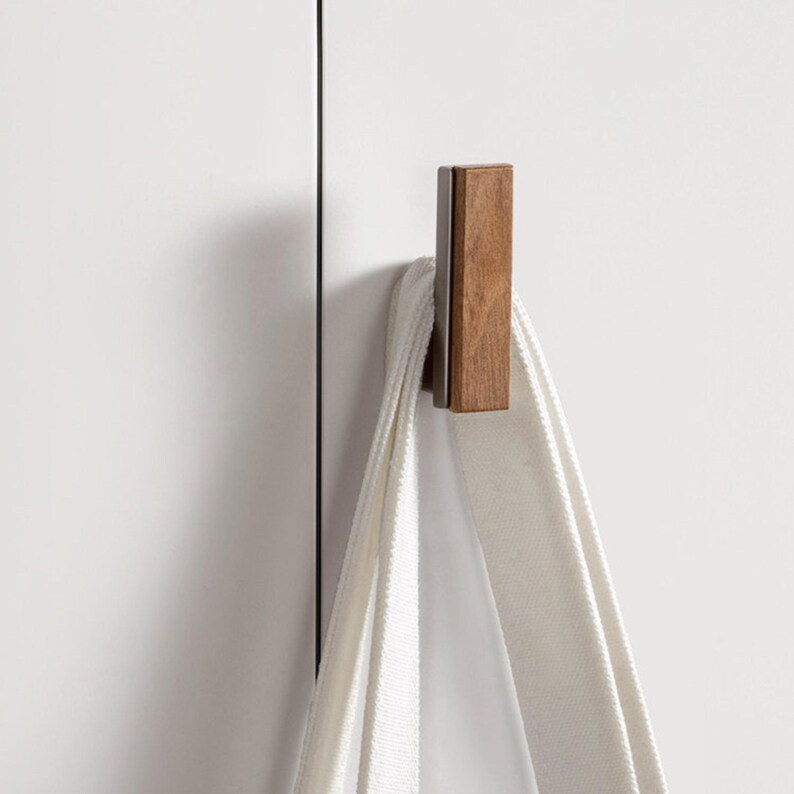 May include: A rectangular wooden hook with a dark brown finish is mounted on a white surface. A white towel hangs from the hook. The hook is a simple, modern design.