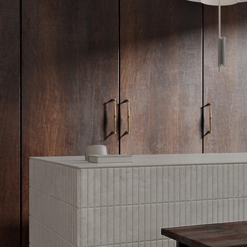 May include: A contemporary kitchen scene with dark wood cupboards and brass handles. A light grey countertop with a textured, vertical tile design is in the foreground. A small white bowl and a book are on the countertop.