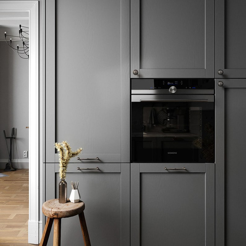 May include: A contemporary kitchen with grey cabinets and an integrated oven. A small wooden stool displays decorative vases and a dried plant. The interior design has a minimalist style, emphasizing functionality and elegance.