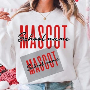 May include: A white crewneck sweatshirt featuring the red text MASCOT in a tall, bold font with the black cursive text School name overlaid. A grey rectangular patch is printed below, also displaying the red MASCOT text and black School name.