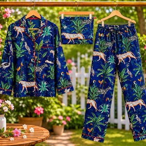 Könnte beinhalten: Ein dreiteiliges Pyjama-Set in leuchtendem Blau mit einem Dschungel-Themen-Print mit Leoparden, Zebras und tropischem Laub. Das Set umfasst ein Hemd mit Knöpfen, eine Hose mit Kordelzug und eine passende Augenmaske, alle mit roter Paspelierung.