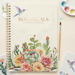 May include: A spiral-bound workbook titled BOTANICALS A WATERCOLOR WORKBOOK with a cream cover featuring a watercolor illustration of a hummingbird and various succulents in shades of green, pink, and yellow, alongside a paintbrush and palette.
