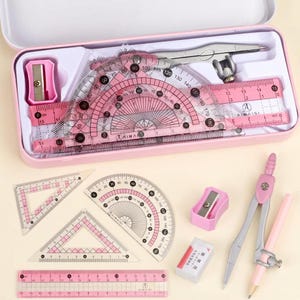 May include: A pink geometry set in a matching rectangular case, including a metal compass, a pink pencil, a pink sharpener, a pink eraser, two triangular rulers, a protractor, and a straight ruler, all featuring clear black measurement markings.