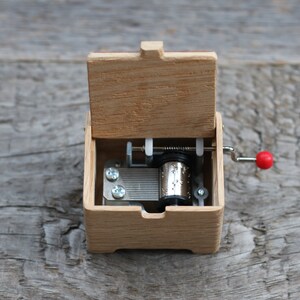 May include: A wooden music box with a red crank and a silver winding mechanism. The lid is open, revealing the inside of the box.