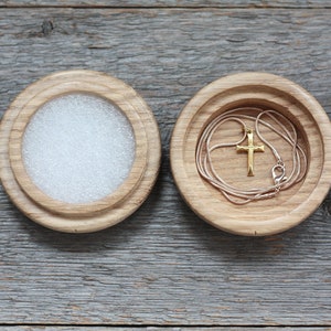 Puede incluir: Una caja de madera con tapa, la tapa est&aacute; abierta y un collar de cadena dorada con un colgante de cruz est&aacute; dentro.