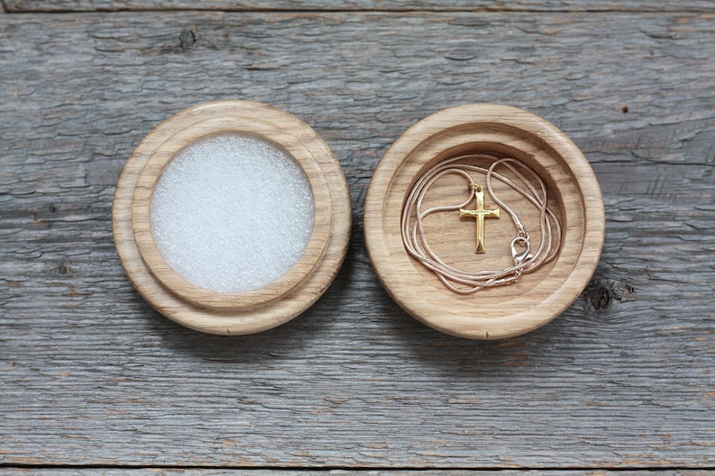 Puede incluir: Una caja de madera con tapa, la tapa est&aacute; abierta y un collar de cadena dorada con un colgante de cruz est&aacute; dentro.