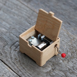 May include: A wooden music box with a crank and a red knob. The lid is open, revealing the inner workings of the music box.