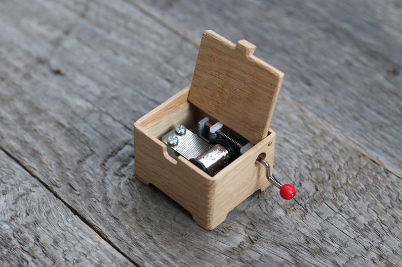May include: A wooden music box with a crank and a red knob. The lid is open, revealing the inner workings of the music box.