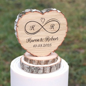 Peut inclure: Un topper de gâteau en bois en forme de cœur avec les initiales "K" et "R" entrelacées dans un symbole d'infini. Le texte "Karen & Robert" et la date "10.03.2025" sont gravés sous le symbole.