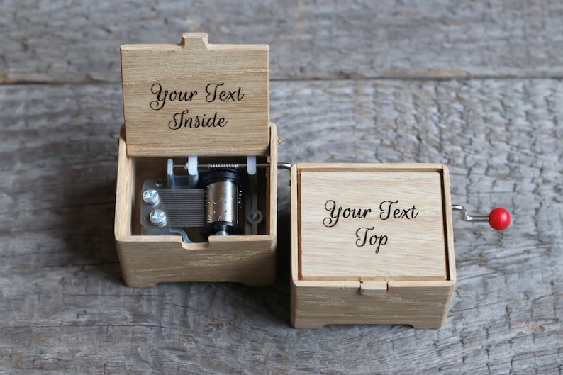 May include: A wooden music box with a hand crank on the side. The top of the box is engraved with the text "Your Text Top". The lid of the box is open, revealing the music mechanism and the text "Your Text Inside" engraved on the inside of the lid.