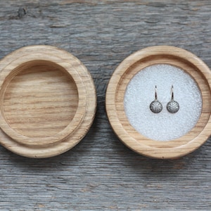 Puede incluir: Un par de pendientes de plata con peque&ntilde;as piedras redondas y transparentes engastadas en un dise&ntilde;o floral. Los pendientes se muestran en una caja de madera con un forro blanco.