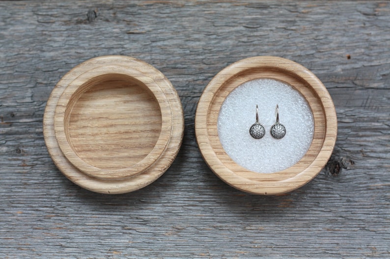 Puede incluir: Un par de pendientes de plata con peque&ntilde;as piedras redondas y transparentes engastadas en un dise&ntilde;o floral. Los pendientes se muestran en una caja de madera con un forro blanco.