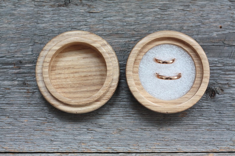 Puede incluir: Dos alianzas de oro en una caja de anillos de madera con un interior de terciopelo blanco.