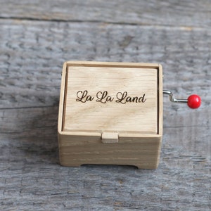 May include: A wooden music box with a red crank and the words "La La Land" engraved on the top.